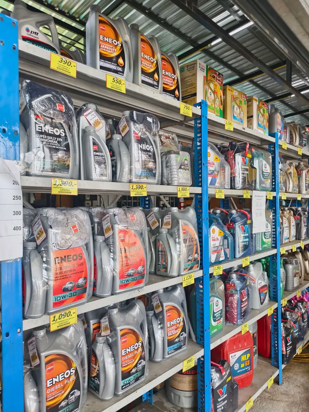 ชั้นวางน้ำมันเครื่องในร้าน มีทั้ง ENEOS PTT Shell Castrol และ Valvoline พร้อมป้ายราคา